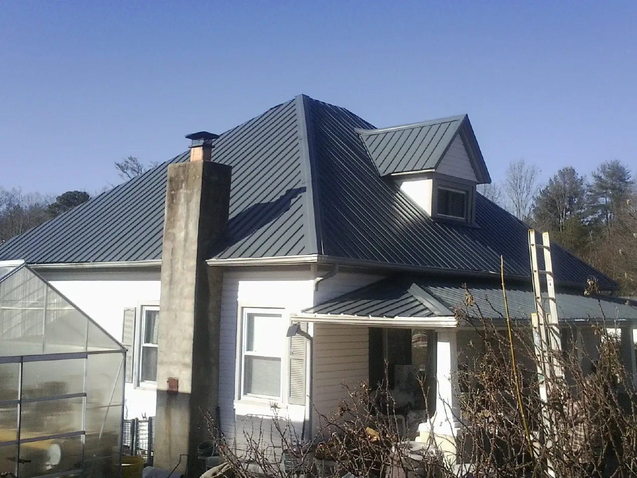 Dark blue standing seam metal roof on a white farmhouse with dormer — Slate & Tile Roof Repair by Roofing Brothers in Alta