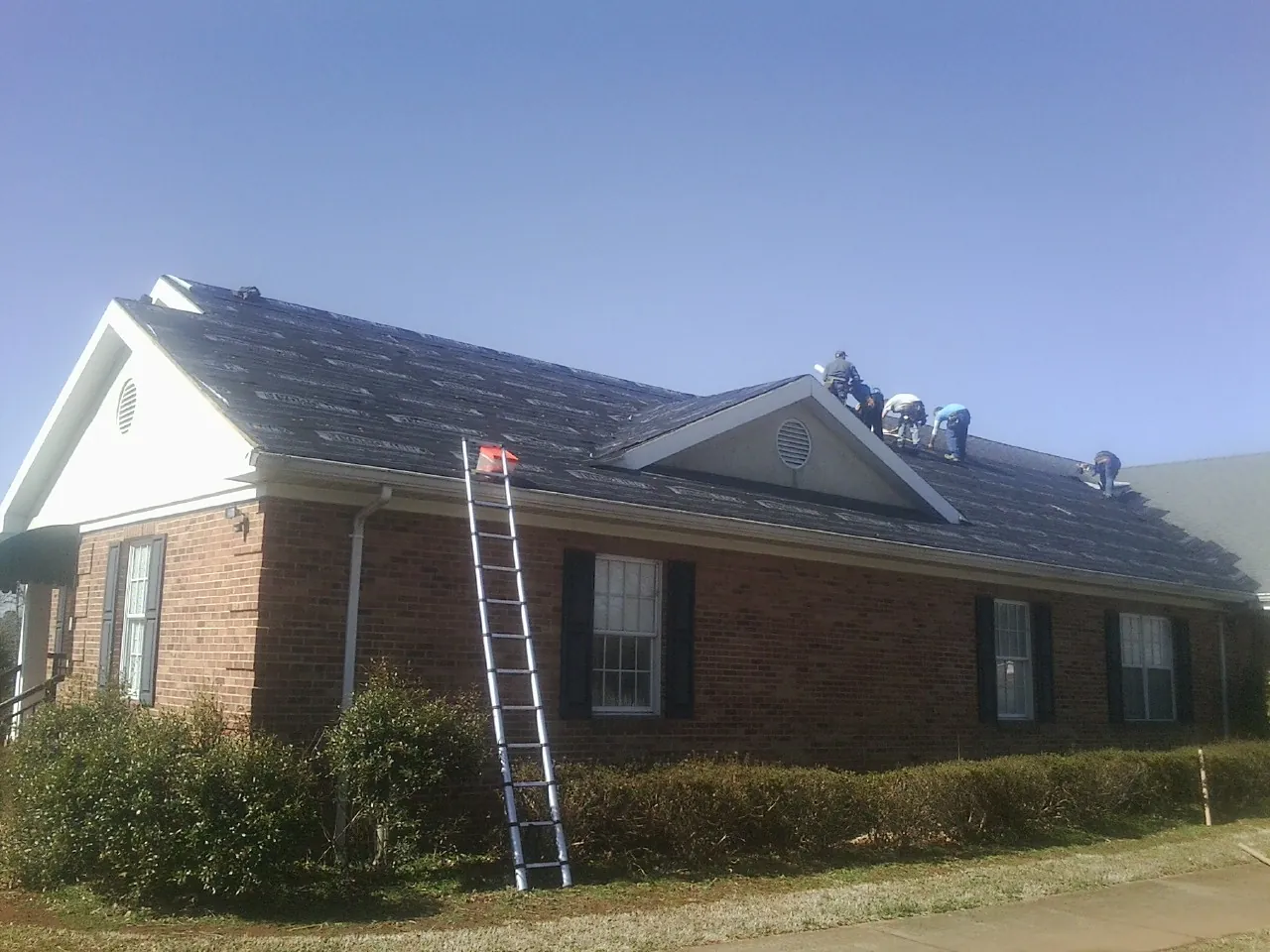 Crew tearing shingles off a brick ranch roof with a ladder set — Metal Roof Repair work by our crew in Alta