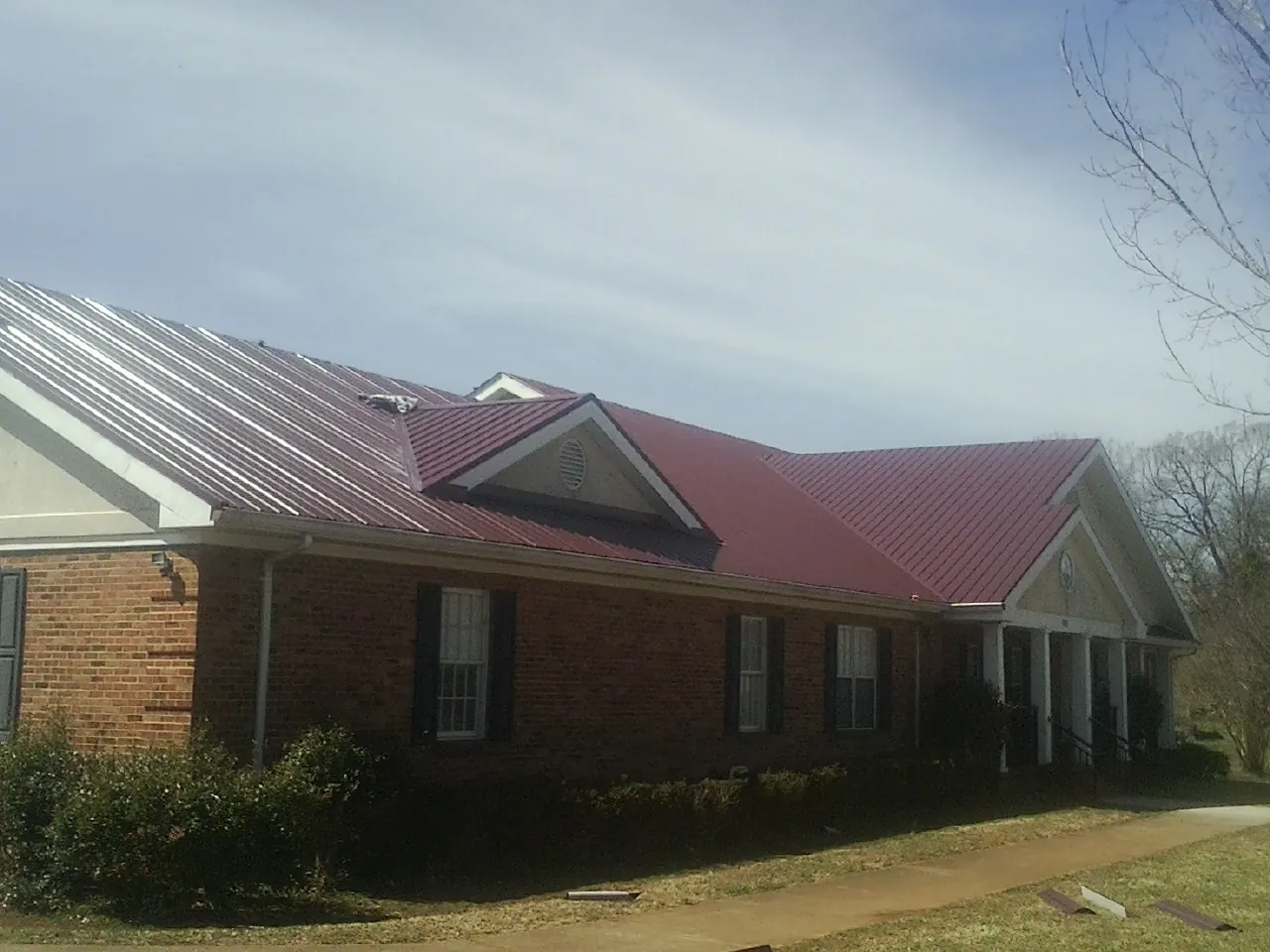 Red metal roof with gabled entries on a long brick building, from a Hail Damage Roof Repair job in Alta