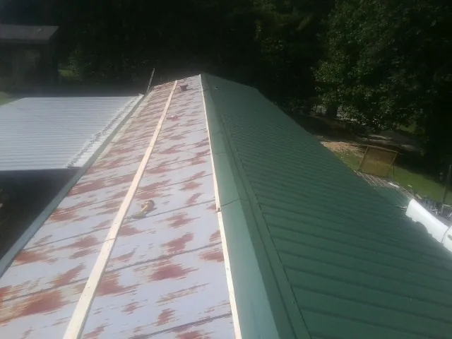 Old rusted panels beside newly installed green metal roofing — Wind Damage Roof Repair by Roofing Brothers in Alta