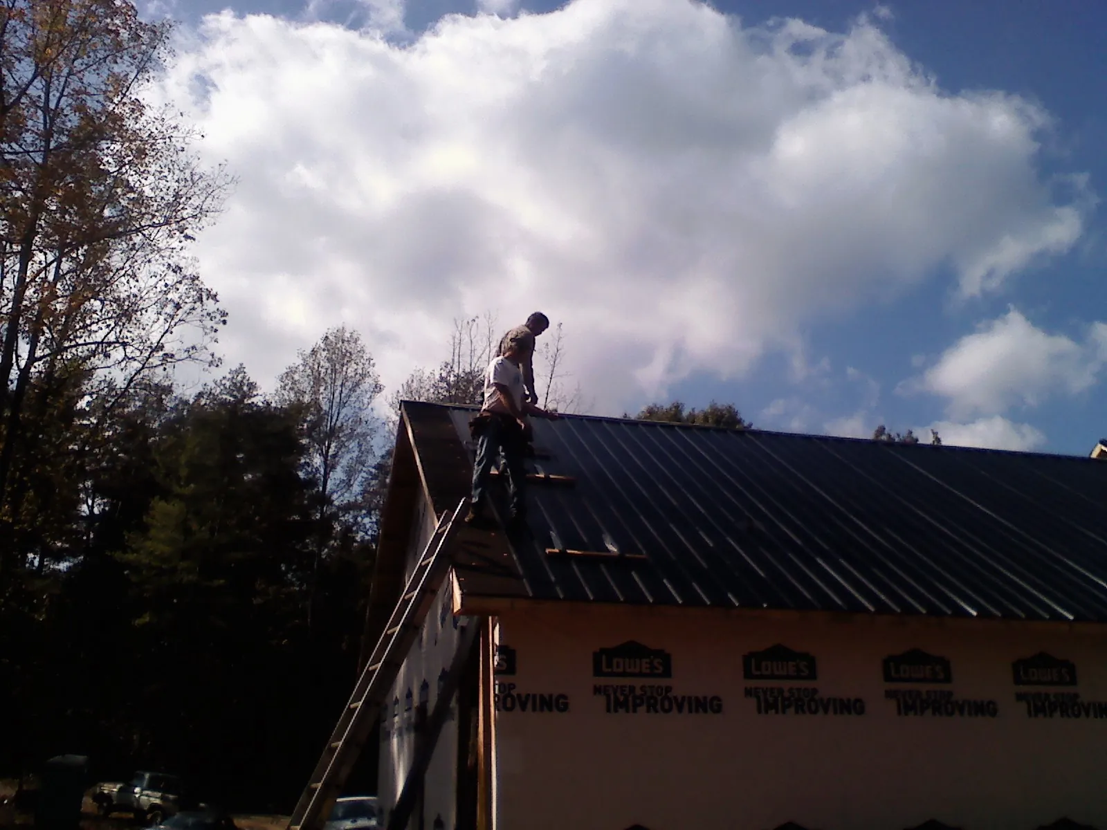 Roofer fastening dark metal panels high against a cloudy sky, from a Roof Inspection job in Alta